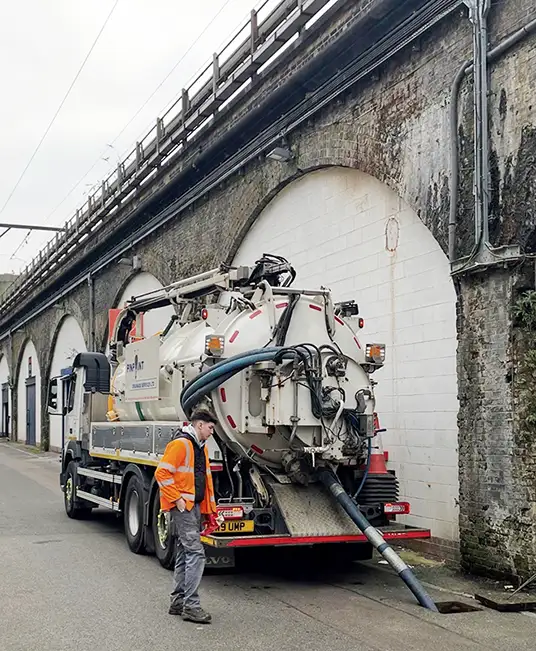 Vacuum tanker carrying out road gully cleaning and highway drainage maintenance beneath a railway arch.